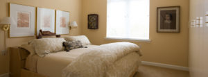 A bedroom in one of Whitney Center's well-appointed apartment homes, featuring sconces, tasteful artwork and a window to allow natural light.