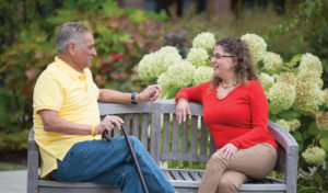 A senior man and younger woman talking together on a park bench