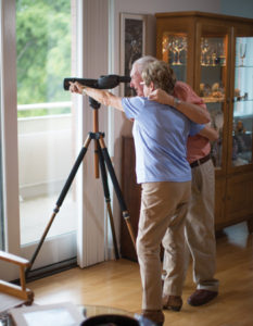 A senior couple look through a telescope, searching for birds on the Whitney Center campus