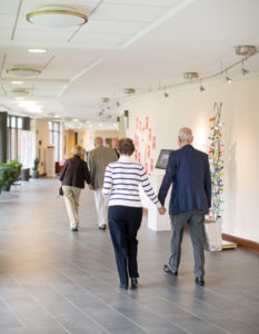 Two senior couples holding hands enjoy the works of art displayed in a Whitney Center hallway gallery