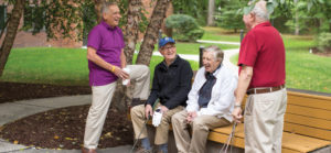 Four senior men holding golf clubs, gathered near a bench