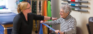 A female physical therapist working with a senior woman who is holding up a blue scarf