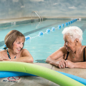 Two senior women relaxing in the water at the edge of a swimming pool