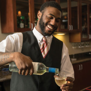A friendly bartender smiles and pours a glass of white wine