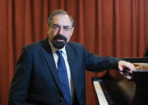 A middle-aged man sitting on a piano bench with his hand resting on top of a piano