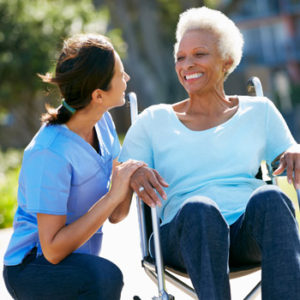 A nurse crouched down, speaking to a senior woman in a wheelchair