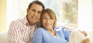 A middle-aged couple smile and pose for a photo in front of a sun-drenched window