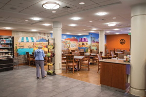 A senior woman picking out a piece of fruit at The Bistro, Whitney Center's casual and take-out dining cafeteria