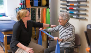 A female physical therapist working with a senior woman who is holding up a blue scarf