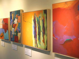 Four colorful framed art pieces displayed on a gallery wall