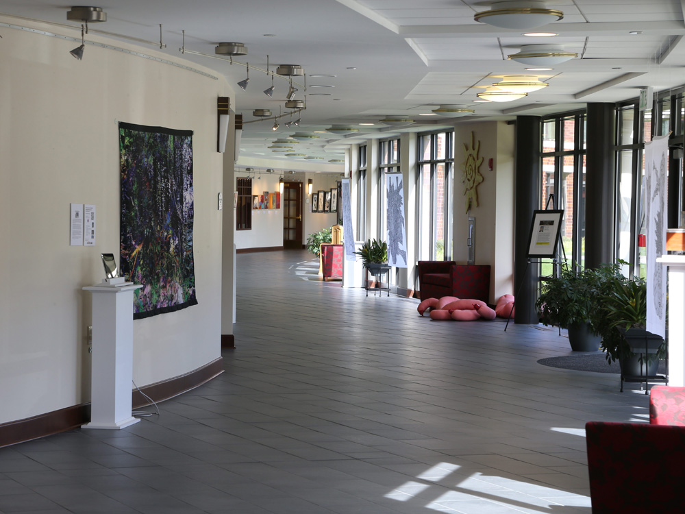 A hallway at Whitney Center, with works of art displayed on the walls, easels and pedestals