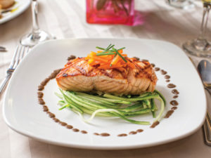 A white dinner plate with a salmon steak, garnished with carrots and greens