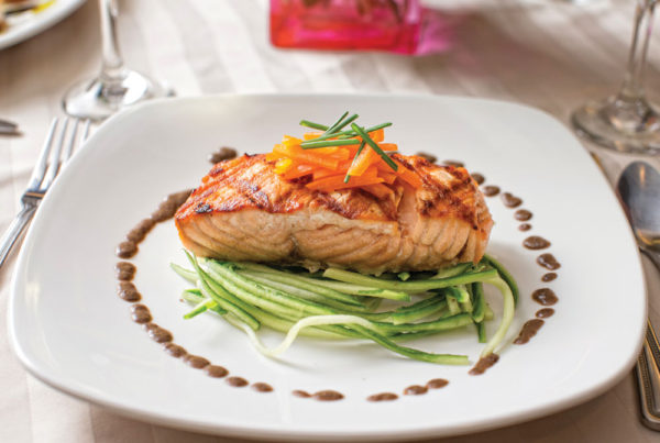 A white dinner plate with a salmon steak, garnished with carrots and greens