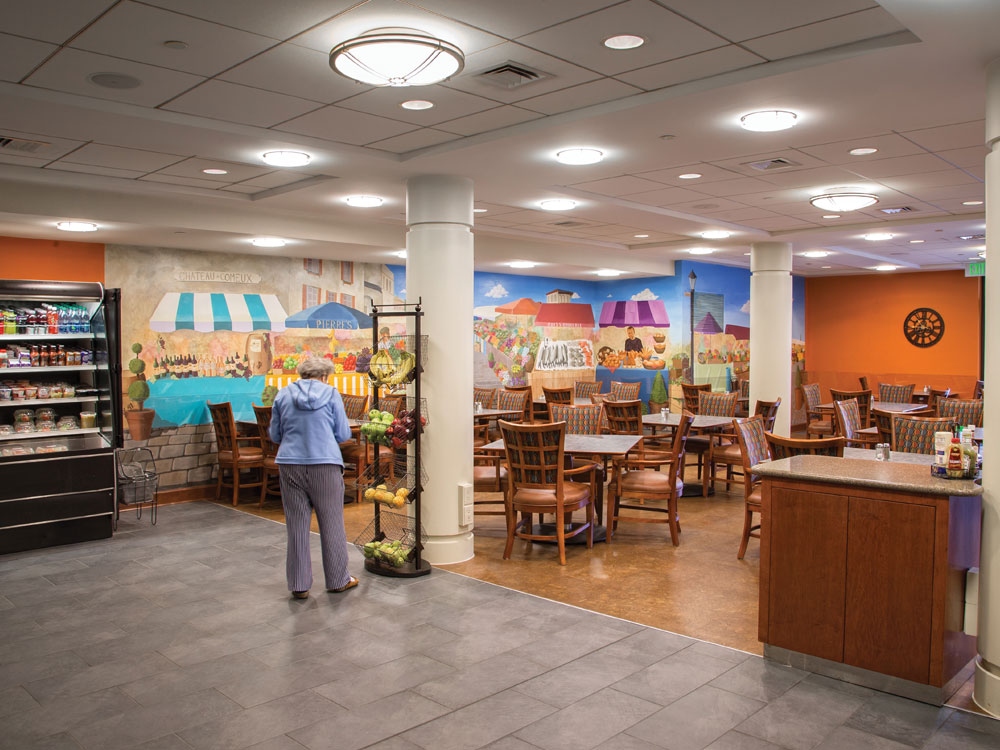 A senior woman picking out a piece of fruit at The Bistro, Whitney Center's casual and take-out dining cafeteria