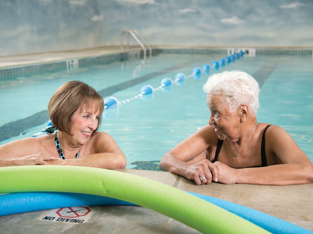 Two senior women relaxing in the water at the edge of a swimming pool