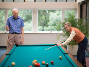 A senior couple playing billiards in a Whitney Center common room
