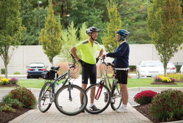 A senior man and woman dressed in bike gear, standing next to bikes and chatting