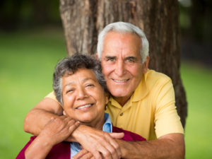 A senior couple smile and pose in front of a tree