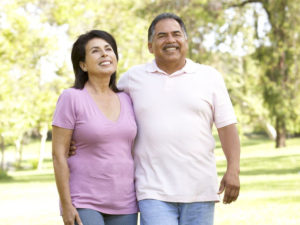 A middle-aged couple smile as they walk in a park-like setting on a summer day