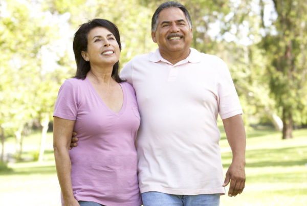 A middle-aged couple smile as they walk in a park-like setting on a summer day