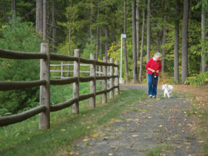 A senior woman walking a small dog on one of Whitney Center's nature trails