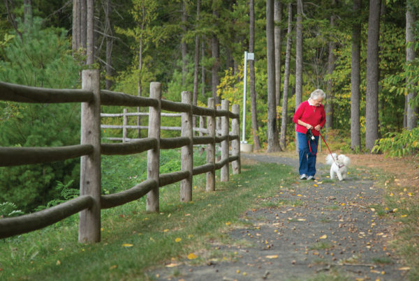 A senior woman walking a small dog on one of Whitney Center's nature trails