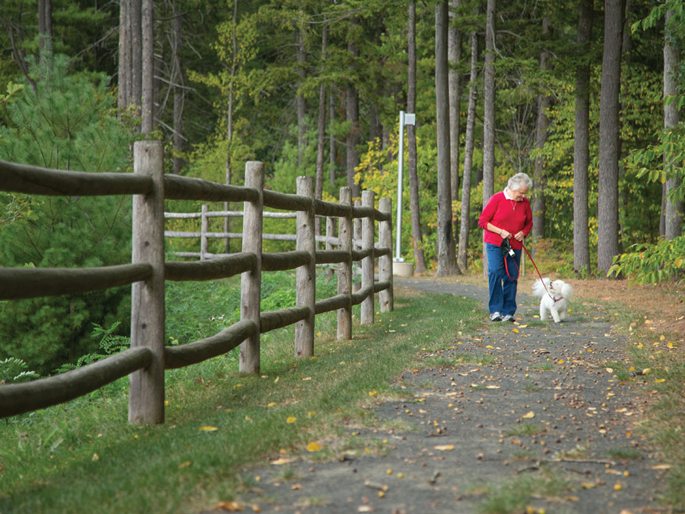 A senior woman walking a small dog on one of Whitney Center's nature trails