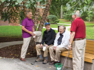 Four senior men holding golf clubs, gathered near a bench