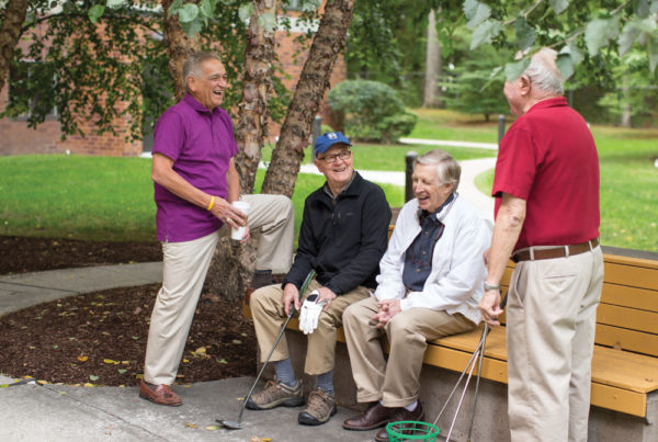 Four senior men holding golf clubs, gathered near a bench