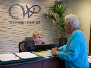 A staff member assists a resident at the front desk of Whitney Center