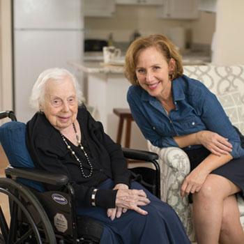 A senior woman with white hair smiles while visiting with a younger female loved one