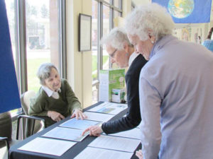 Two senior ladies look over information about Earth Day while a third lady looks on