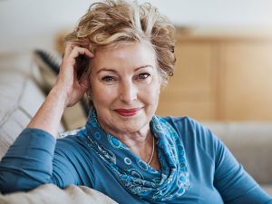 An elegant senior woman, dressed in a gray-blue shirt and scarf, smiles at the camera