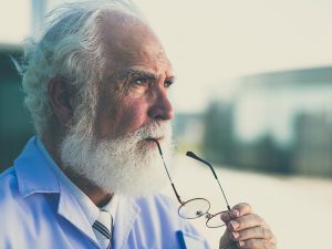 A senior man holding his glasses to his mouth, gazes into the distance