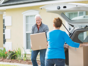 A senior man carries a large cardboard box to a woman putting boxes into a van