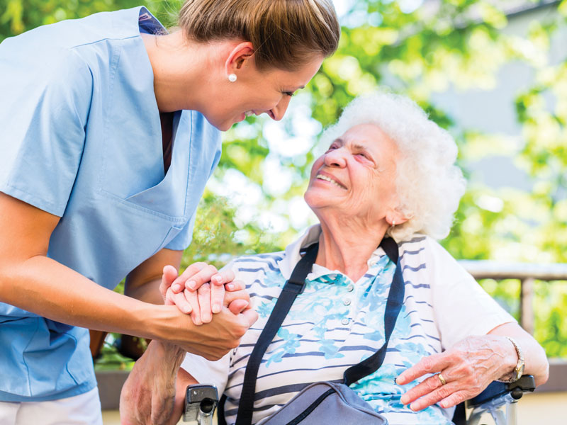 A female staff member smiles and clasps hands with a senior woman