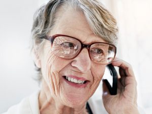 A senior woman wearing glasses, smiling as she talks on a cell phone